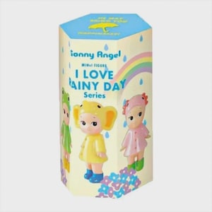 May include: A hexagonal box featuring the "Sonny Angel I Love Rainy Day Series" with three small figurines. The box has a light yellow background with a rainbow and text. The figurines are dressed in rain-themed outfits.