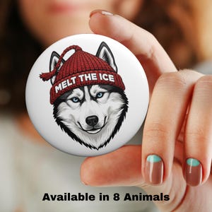 May include: A white button featuring a detailed illustration of a husky dog wearing a red knit cap with the text "Melt the Ice." The button also includes the text "Available in 8 Animals."