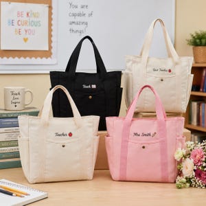 May include: Four canvas tote bags in black, cream, and pink, with side pockets and handles. Each bag is embroidered with text: "Teach," "Teacher," "Best Teacher," and "Mrs. Smith." The bags have a button closure.