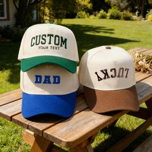 Könnte beinhalten: Drei Baseballkappen mit individuellem Text. Eine Kappe hat "CUSTOM" und "YOUR TEXT" in Grün, eine andere "DAD" in Blau und die dritte "LUCKY" in Braun. Die Kappen sind beige mit farbigen Schirmen.