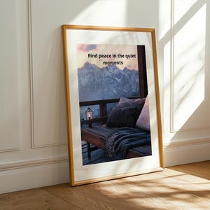 Könnte beinhalten: Ein gerahmter Druck mit dem Text "Find peace in the quiet moments" über einer Berglandschaft. Das Bild zeigt eine gemütliche Szene im Freien mit Kissen, einer Decke und einer Laterne.