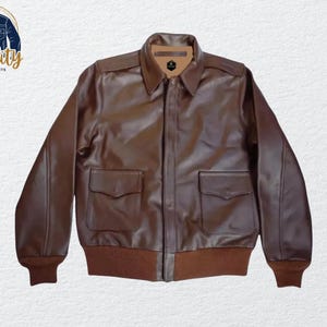 Könnte beinhalten: Braune Lederjacke mit Kragen und zwei Vordertaschen. Die Jacke hat einen Reißverschluss und gerippte Bündchen und Saum. Das Logo "Quality One Jackets" befindet sich in der oberen linken Ecke.