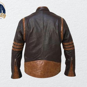 May include: A brown and tan leather jacket with a classic design. The jacket features brown stripes on the sleeves and a brown lower panel. The jacket has a zipper closure on the sleeves and a collar. The logo "Quality One Jackets" is in the upper left corner.