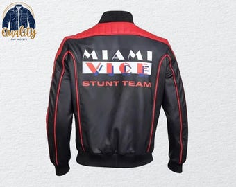 Może przedstawiać: Czarna kurtka bomberka z czerwonymi akcentami i napisem "MIAMI VICE STUNT TEAM" na plecach. Kurtka ma czarny kołnierz i mankiety. Czerwone paski biegną wzdłuż rękawów.