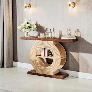 Könnte beinhalten: Eine moderne Holzkonsolentisch mit einer dunkelbraunen Ober- und Unterseite und einer hellbraunen, kreisförmigen Mitte mit offenen Regalen. Der Tisch ist mit einer Vase mit weißen Blumen, Büchern und Flaschen dekoriert.