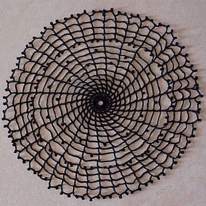 May include: A black crocheted doily with a spiral design. The doily is circular and has a delicate, lacy appearance.