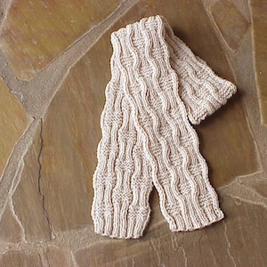 May include: A beige knitted scarf with a textured pattern. The scarf is folded in half and laid on a stone surface.