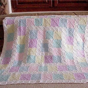 May include: A crocheted baby blanket with a patchwork design in pastel colors of pink, blue, yellow, and white.