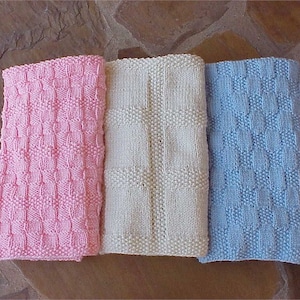 May include: Three knitted baby blankets in pink, white, and light blue. Each blanket has a woven pattern.