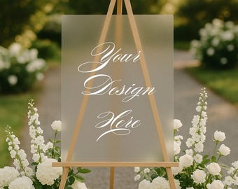 Könnte beinhalten: Ein klares Acrylschild auf einer Holzstaffelei mit dem Schriftzug "Your Design Here" in Weiß. Das Schild ist von weißen Blumen umgeben, ideal für Veranstaltungen.
