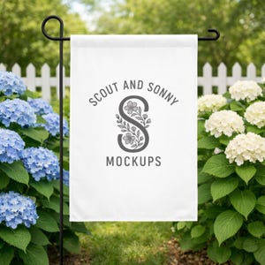 May include: A white garden flag with the text "SCOUT AND SONNY MOCKUPS" in gray. The flag is hanging on a black metal stand, surrounded by blue and white flowers and green foliage.