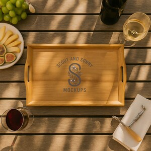 May include: A rectangular wooden serving tray with handles, featuring the text "SCOUT AND SONNY MOCKUPS" in a circular design. The tray is surrounded by food and drinks, including grapes, cheese, figs, wine, and a wine glass.