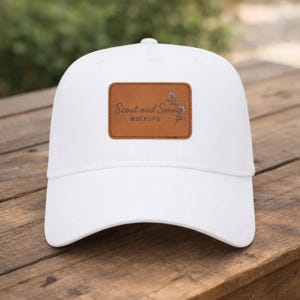 May include: A white baseball cap with a brown leather patch. The patch features the text "Scout and Sonny Mockups" and a floral design. The cap is on a wooden surface.