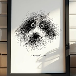 Puede incluir: Lámina artística enmarcada con una ilustración garabateada y angustiada de la cara de un perro con ojos grandes y expresivos. El texto "It wasn't me" está impreso debajo de la imagen. La obra está enmarcada en negro.