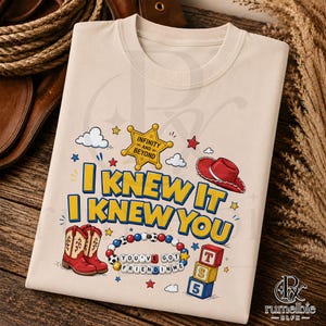 May include: A beige t-shirt featuring a graphic print with the text I KNEW IT I KNEW YOU, a yellow sheriff star with INFINITY AND BEYOND, a red cowboy hat, a pair of red and beige cowboy boots, a beaded bracelet with YOU'VE GOT A FRIEND IN ME, and blocks.
