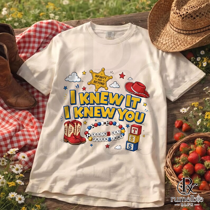 May include: A cream-colored t-shirt featuring a graphic print with the text "I KNEW IT I KNEW YOU" in yellow and blue. The design includes a gold sheriff badge, a red cowboy hat, red cowboy boots, a beaded bracelet, and three stacked blocks.
