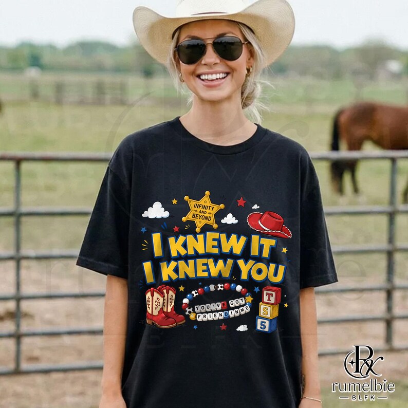 May include: A black short-sleeved t-shirt featuring a graphic print with the text I KNEW IT I KNEW YOU, a yellow sheriff star badge with the text INFINITY AND BEYOND, a red cowboy hat, red cowboy boots, a beaded necklace, and three stacked blocks.