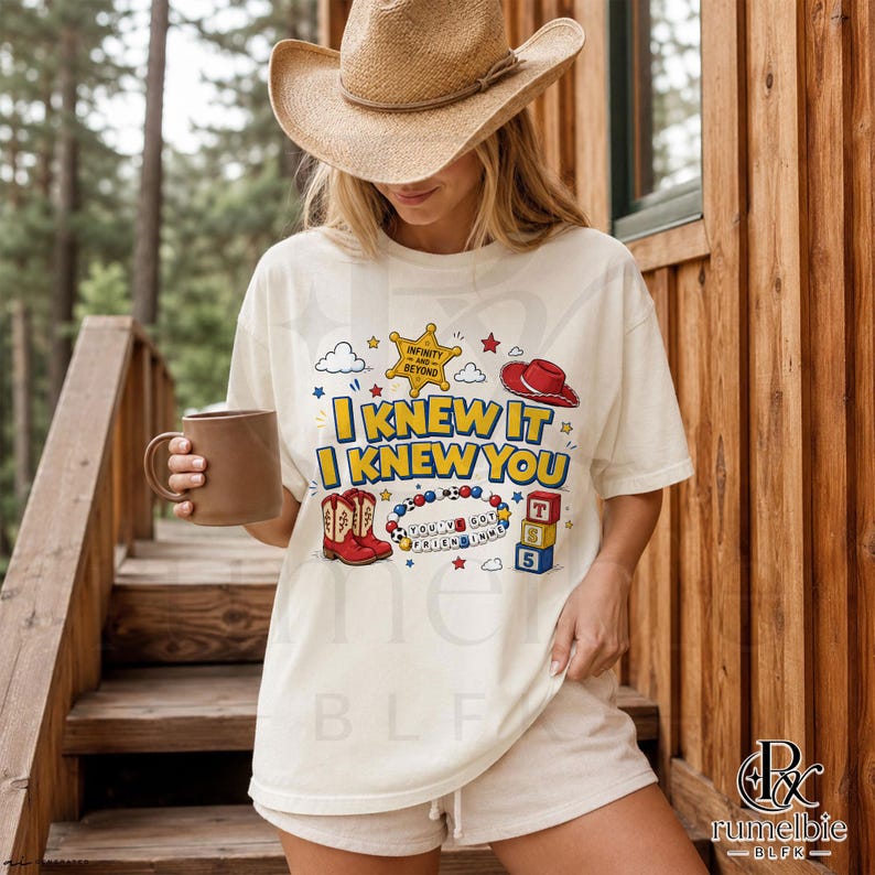 May include: An off-white short-sleeve t-shirt featuring a graphic print with the text I KNEW IT I KNEW YOU, a yellow sheriff badge, a red cowboy hat, red cowboy boots, a beaded bracelet with the text YOU'VE GOT A FRIEND IN ME, and blocks.