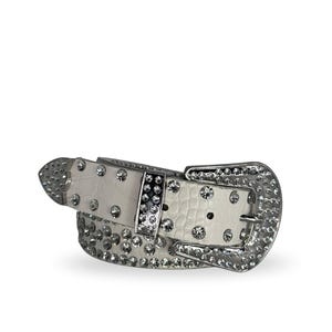 May include: White belt with a silver-tone buckle and crystal embellishments. The belt has a crocodile-effect leather strap and is decorated with many clear rhinestones. The buckle and tip are also covered in rhinestones.