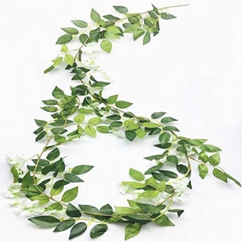 May include: A decorative garland featuring green leaves and small white flowers. The leaves are a vibrant green, and the flowers add a touch of delicate white. The garland is designed to be draped or hung for decoration.