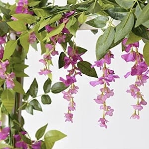 May include: Artificial wisteria garland with cascading purple flowers and green leaves. The flowers are a vibrant shade of purple, and the leaves are a deep green. The garland is designed for decorative purposes.