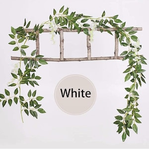 May include: A decorative garland featuring green leaves and white flowers, draped over a rustic wooden ladder. The word "White" is displayed in a white circle. Ideal for home decor or event styling.