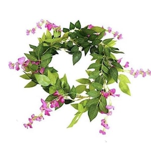 May include: A circular floral wreath featuring vibrant green leaves and delicate pink flowers. The wreath is artfully arranged, creating a natural and decorative element. Perfect for adding a touch of spring to any space.