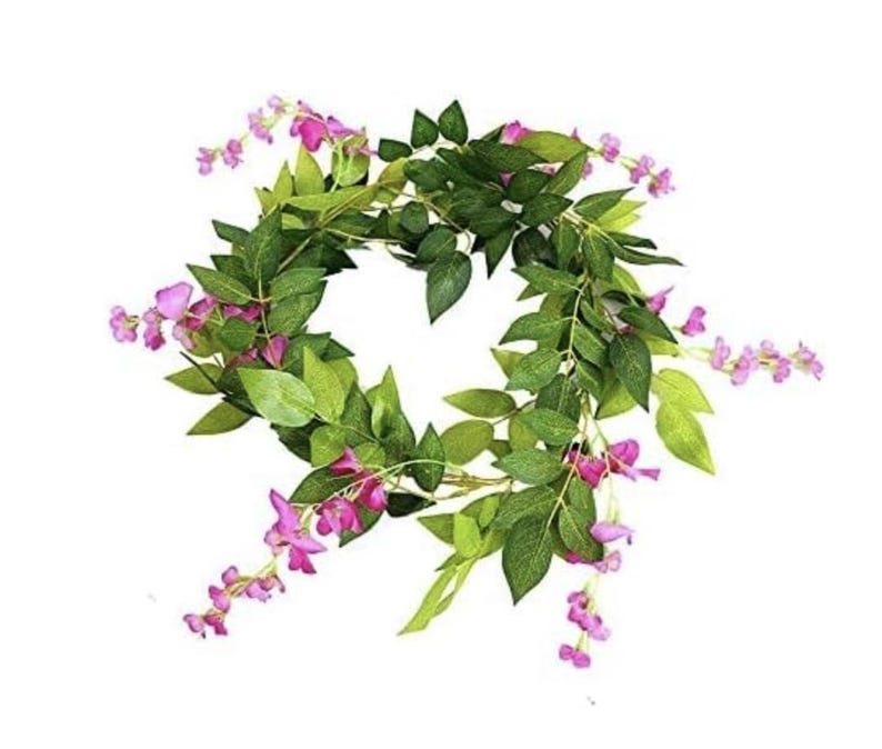 May include: A circular floral wreath featuring vibrant green leaves and delicate pink flowers. The wreath is artfully arranged, creating a natural and decorative element. Perfect for adding a touch of spring to any space.