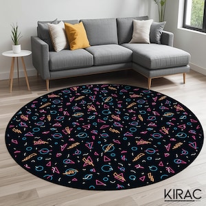 Op de afbeelding: Een ronde zwarte vloerkleed met een retro jaren 80 design. Het vloerkleed heeft een herhalend patroon van roze, blauwe en gele geometrische vormen, waaronder driehoeken, bliksemschichten en cirkels. Het vloerkleed ligt op een lichte houten vloer.