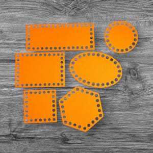 Könnte beinhalten: Eine Auswahl an orangefarbenen geometrischen Formen mit gleichmäßig verteilten Löchern an den Rändern. Die Formen umfassen Rechtecke, Quadrate, ein Oval, einen Kreis und ein Sechseck. Die Objekte sind auf einer grau-schwarzen Holzoberfläche angeordnet.