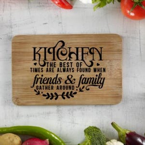 May include: A rectangular wooden cutting board with the word "KITCHEN" in a decorative font. The text "THE BEST OF TIMES ARE ALWAYS FOUND WHEN friends & family GATHER AROUND" is also printed on the board. Vegetables surround the board.