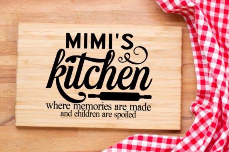 May include: A rectangular wooden cutting board with the words "MIMI'S kitchen" in black script. Below the text is a rolling pin graphic and the phrase "where memories are made and children are spoiled." A red and white checkered cloth is in the background.
