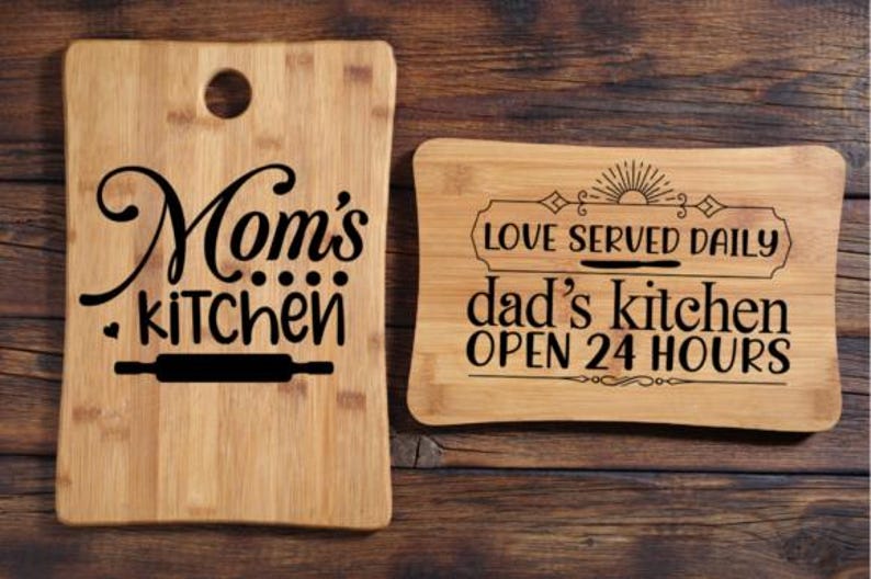 May include: Two wooden cutting boards with black text. One says "Mom's kitchen" with a rolling pin graphic. The other says "Love served daily dad's kitchen OPEN 24 HOURS" with a sun graphic.
