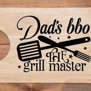 May include: Wooden cutting board with a handle, featuring the text "Dad's bbq the grill master" in black. The design includes crossed spatula and fork illustrations, and star accents.