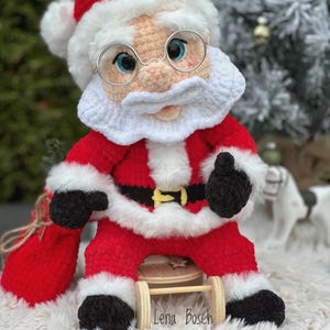 Pode incluir: Boneca de croch&ecirc; feita &agrave; m&atilde;o do Papai Noel, vestindo um terno vermelho com acabamento branco, um chap&eacute;u combinando e &oacute;culos redondos. A boneca tem barba e bigode brancos, luvas pretas e est&aacute; segurando um saco vermelho. O nome "Lena Bosch" est&aacute; na base.