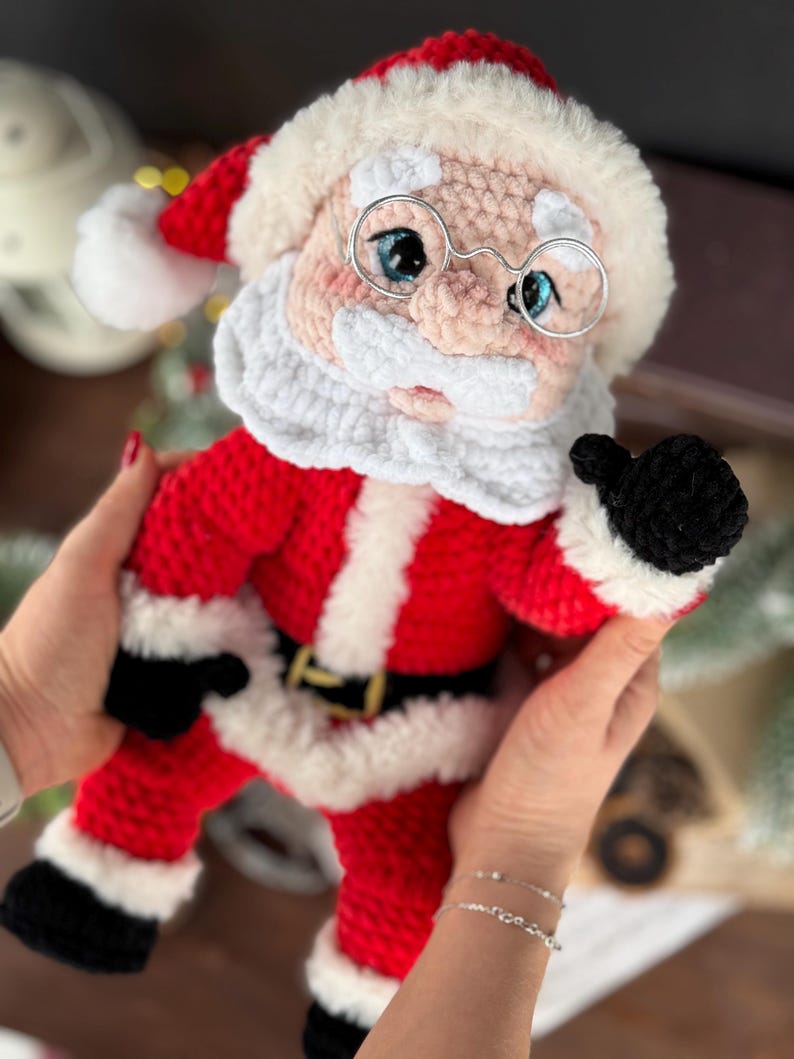 Pode incluir: Boneca de Papai Noel de croch&ecirc;, vestida de vermelho e branco com cinto e luvas pretas. A boneca tem uma barba branca fofa, um chap&eacute;u vermelho e &oacute;culos com arma&ccedil;&atilde;o de arame. Uma decora&ccedil;&atilde;o de Natal encantadora.