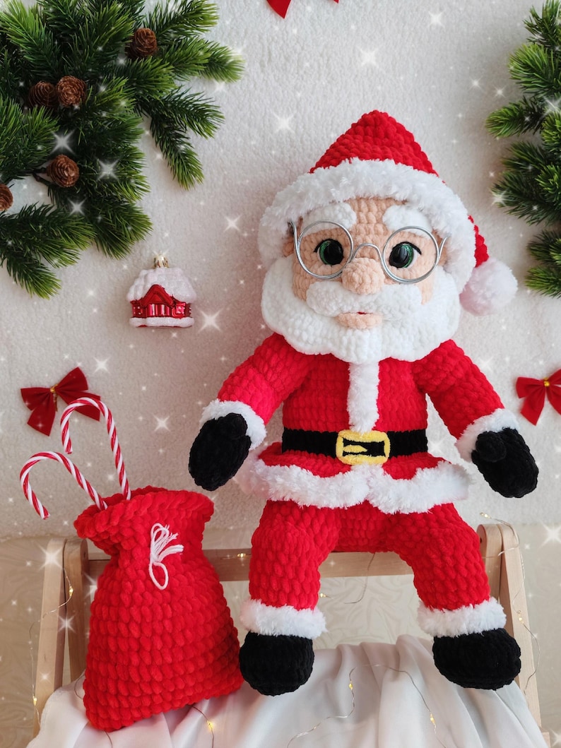 Pode incluir: Boneca de croch&ecirc; feita &agrave; m&atilde;o do Papai Noel, vestindo um terno vermelho com acabamento branco, um cinto preto com fivela dourada e botas pretas. A boneca tem barba branca, &oacute;culos e um chap&eacute;u vermelho. Uma sacola vermelha com bengalas doces est&aacute; por perto.
