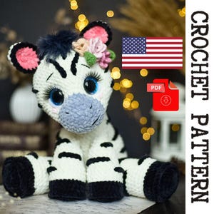 Puede incluir: Un peluche de cebra hecho a mano con ganchillo, con cuerpo blanco y rayas negras. La cebra tiene grandes ojos azules, orejas forradas de rosa y una nariz azul. Está adornada con una corona floral. La imagen incluye el texto "CROCHET PATTERN" y la bandera estadounidense.