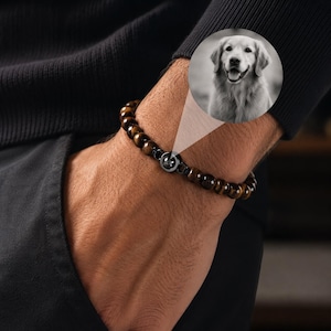 Könnte beinhalten: Ein Armband mit braunen Tigeraugen-Perlen und einem silberfarbenen Anhänger. Der Anhänger zeigt ein Hunde-Gesicht. Das Armband wird am Handgelenk getragen.