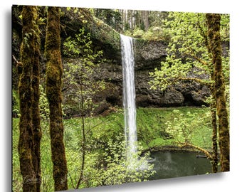 Könnte beinhalten: Landschaftsfotografie eines Wasserfalls, der eine felsige Klippe hinunterstürzt. Das Bild zeigt üppiges grünes Laub, moosbedeckte Bäume und einen ruhigen Wasserpool am Fuße der Wasserfälle. Die Szene wird von Bäumen eingerahmt.
