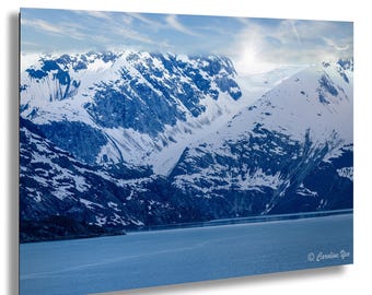 May include: A scenic landscape photograph featuring snow-covered mountains under a cloudy sky. The mountains are a deep blue, contrasted by the white snow. A body of water is in the foreground, reflecting the sky's blue hues.