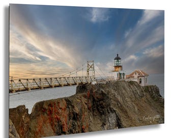 May include: A scenic photograph of a lighthouse on a rocky cliff, connected by a bridge. The sky is filled with dramatic clouds. The lighthouse is white with a black top, and a small building is attached. The bridge is white and connects to the cliff.