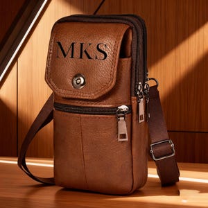 May include: A brown leather crossbody bag with a flap closure and a shoulder strap. The bag features the initials "MKS" on the front. It has multiple zippered compartments and a buckle on the strap.