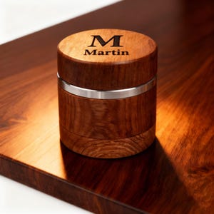 May include: A cylindrical wooden box with a silver band, engraved with the name "Martin" and the letter "M" on the lid. The box is made of dark brown wood and sits on a matching wooden surface.