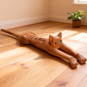 May include: A wooden cat figurine in a stretching pose, with the text "I'm itchy" carved on its side. The cat is light brown and has outstretched paws. The figurine is on a wooden floor.