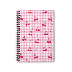 May include: A spiral-bound notebook featuring a pink gingham pattern with red cherries and small hearts. The notebook's cover is a cheerful design, perfect for note-taking or journaling. The spiral binding is black.