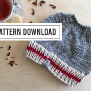 May include: A gray knit beanie with a cream-colored brim featuring red stripes. The text "PATTERN DOWNLOAD" is displayed in a white rectangle. A teacup and cookies are in the background.