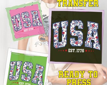 May include: DTF transfer designs featuring the word "USA" in a floral pattern, with "EST. 1776" below. The designs are on pink, green, and black backgrounds. The text "DTF TRANSFER" and "READY TO PRESS" are also visible.
