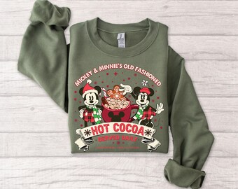 May include: Olive green sweatshirt featuring Mickey and Minnie Mouse with a holiday design. The graphic includes the text "Mickey & Minnie's Old Fashioned Hot Cocoa Served Daily" with festive illustrations of the characters and hot cocoa.