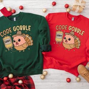 May include: Two sweatshirts, one green and one red, each featuring a cartoon turkey wearing a hat and holding a gravy bag. The text "CODE GOBBLE" is above the turkey. Festive holiday-themed apparel.